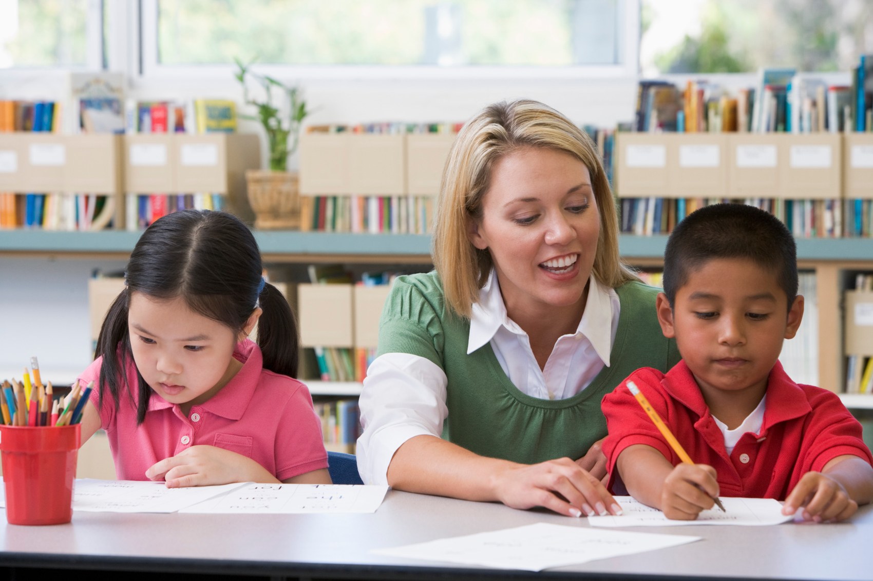 Teacher helping two pupils with their writing in a classroom