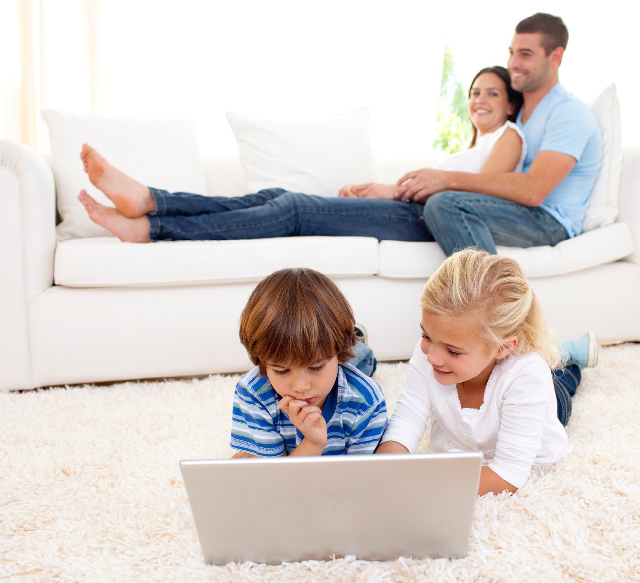 Children using a laptop with their parents nearby
